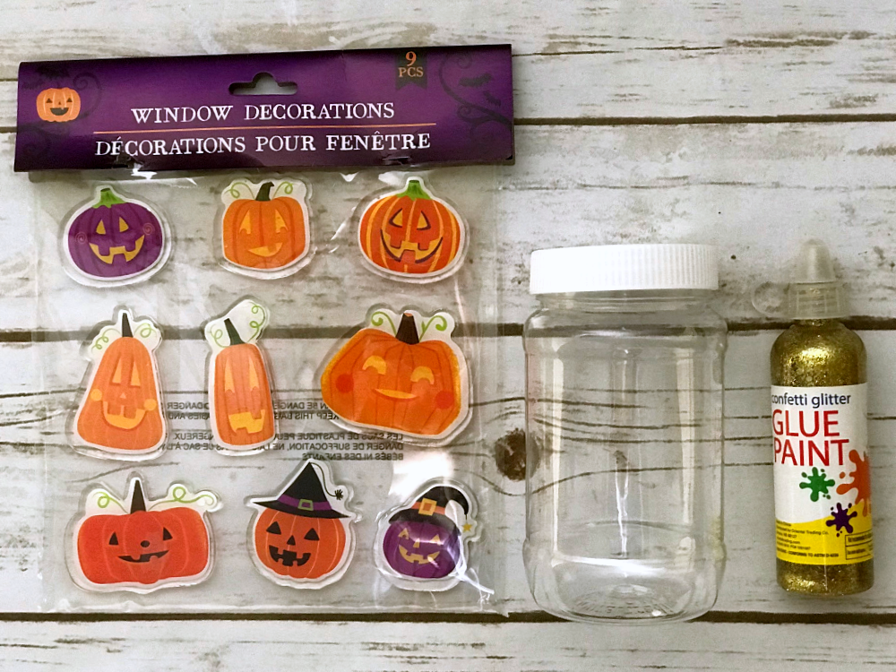supplies needed for this fall craft for kids including pumpkin window gel clings, a clear plastic jar with a lid, and a bottle of gold glitter glue.