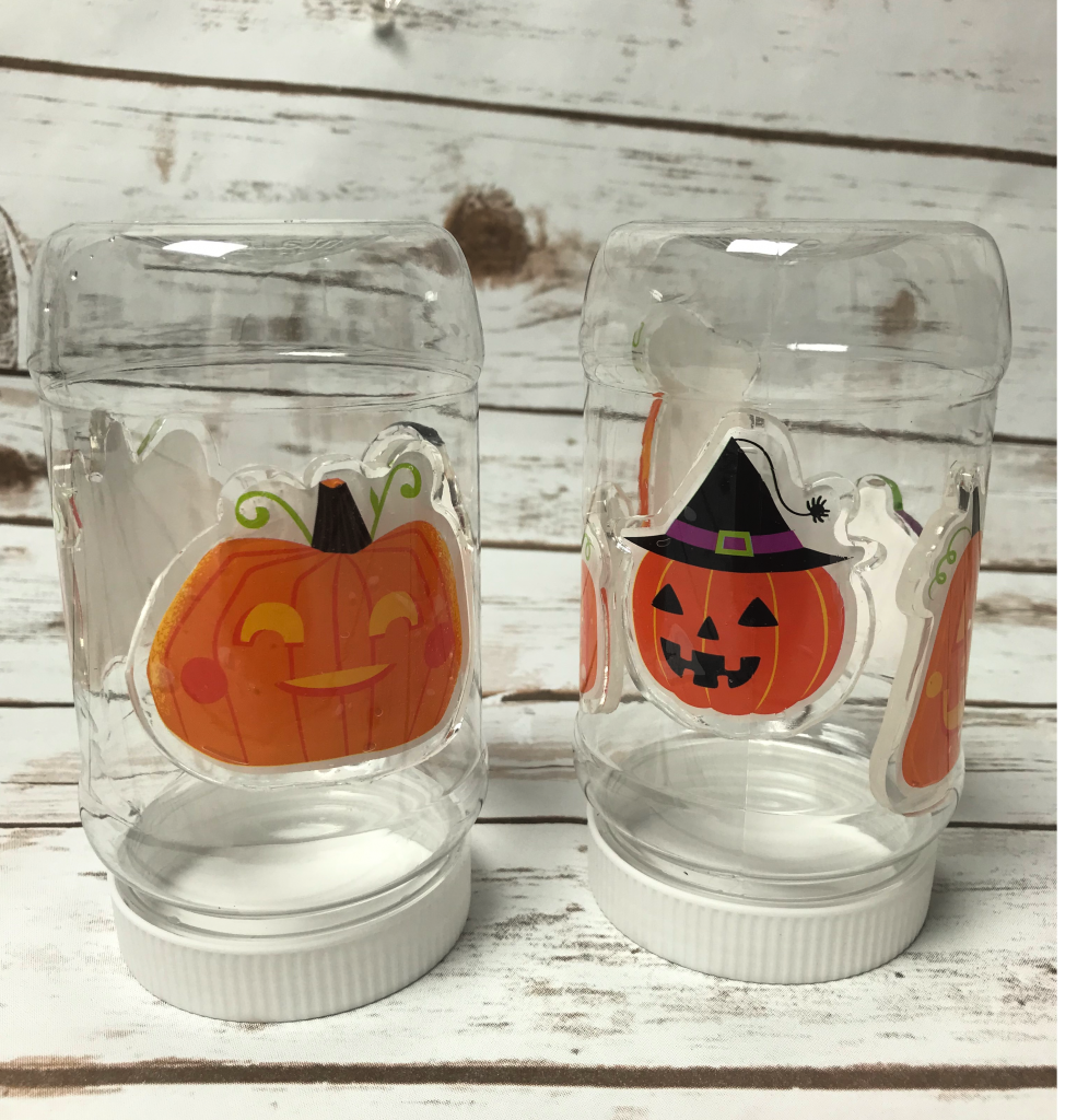 two clear jars with lids with the pumpkin gel clings pressed inside the jars for the snow globe activity