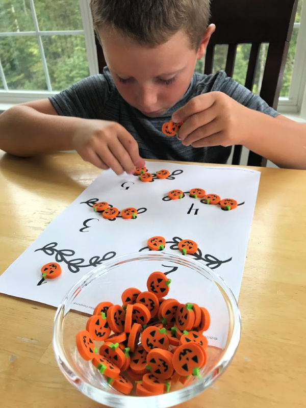 A young boy placing mini pumpkin erasers on the pumpkin math activity printable