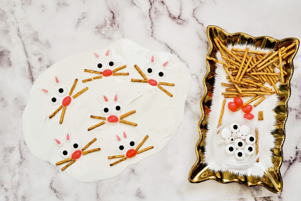 Easter bunny bark ingredients to include pretzel sticks, pink jelly beans, candy eyes, and melted which chocolate