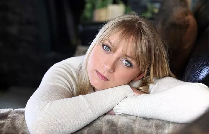A woman with wispy bangs posing on her sofa