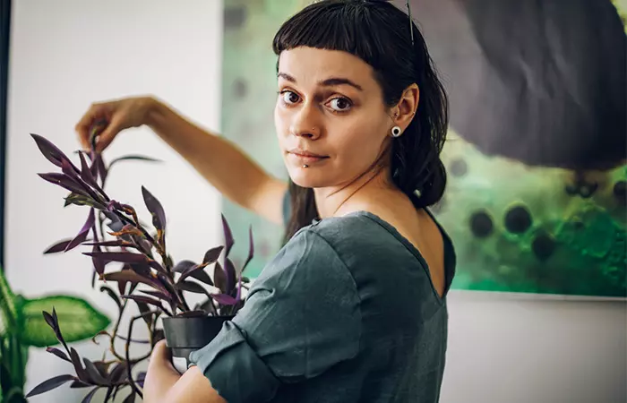 A happy woman with short bangs holding a plant in her home garden