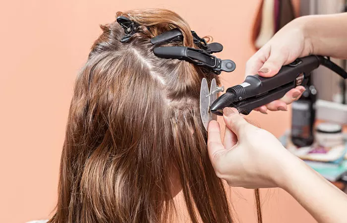 A woman getting a quick weave done with the help of bonding glue at a hair salon.